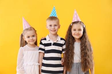 Photo of Children in conical paper hats on yellow background. Birthday surprise party