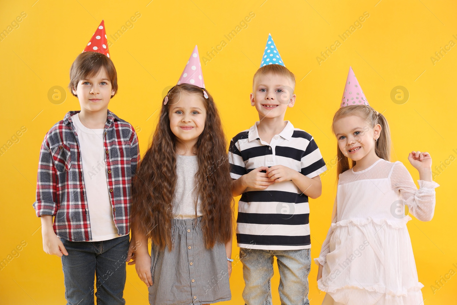 Photo of Children in conical paper hats on yellow background. Birthday surprise party