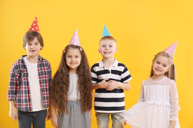 Photo of Children in conical paper hats on yellow background. Birthday surprise party