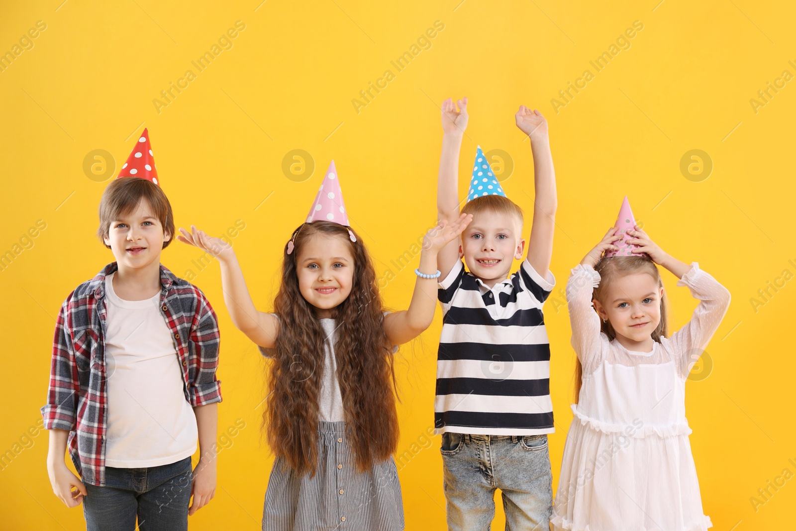 Photo of Children in conical paper hats on yellow background. Birthday surprise party