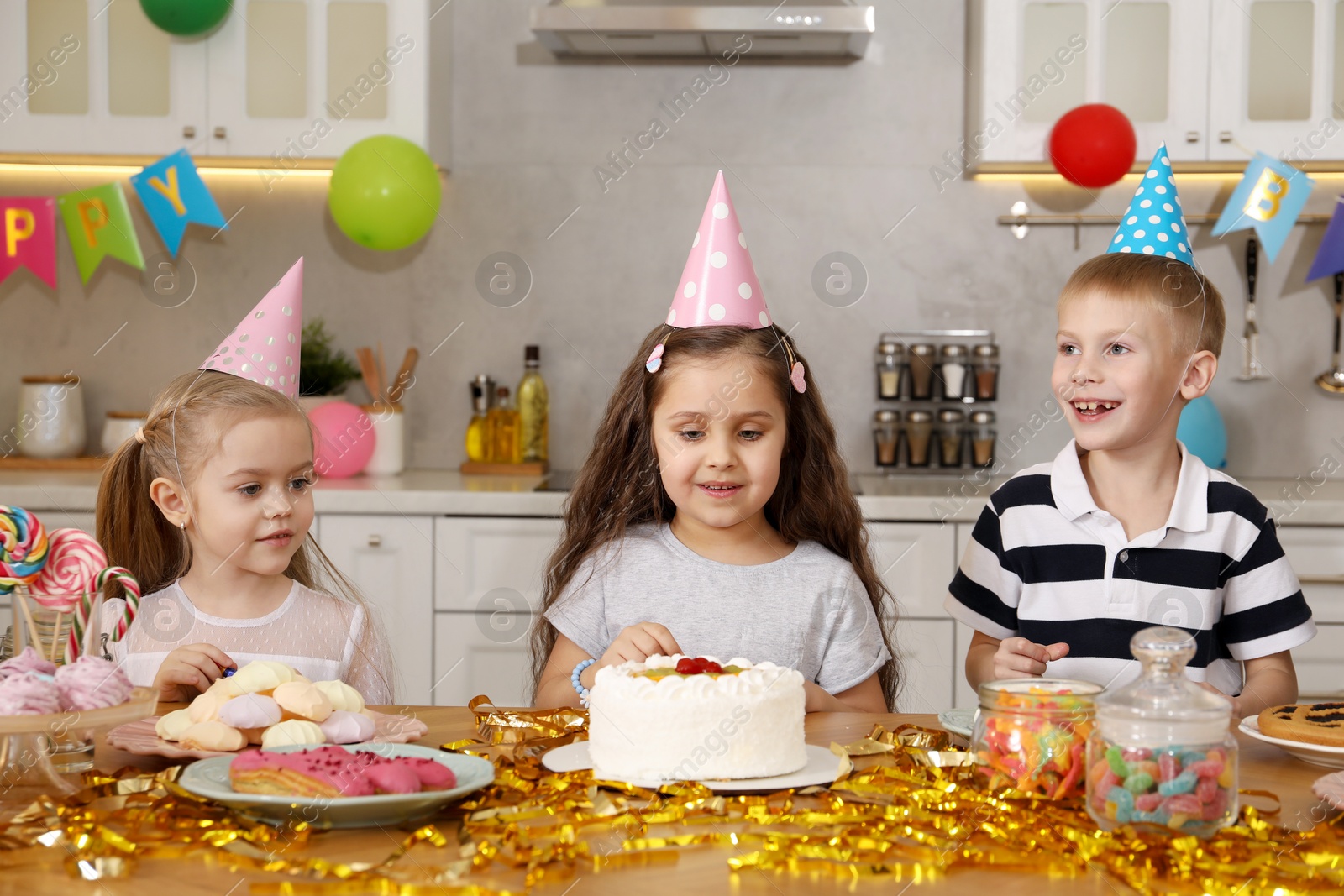 Photo of Children at table with tasty cake and different treats indoors. Surprise party