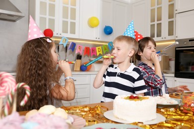 Photo of Children in conical paper hats with blowers celebrating birthday indoors. Surprise party