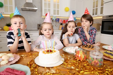 Photo of Children at table with tasty cake and different treats indoors. Surprise party