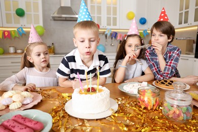 Photo of Children at table with tasty cake and different treats indoors. Surprise party