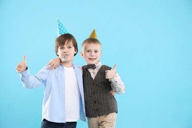 Photo of Children in conical paper hats with blower on light blue background, space for text. Birthday surprise party