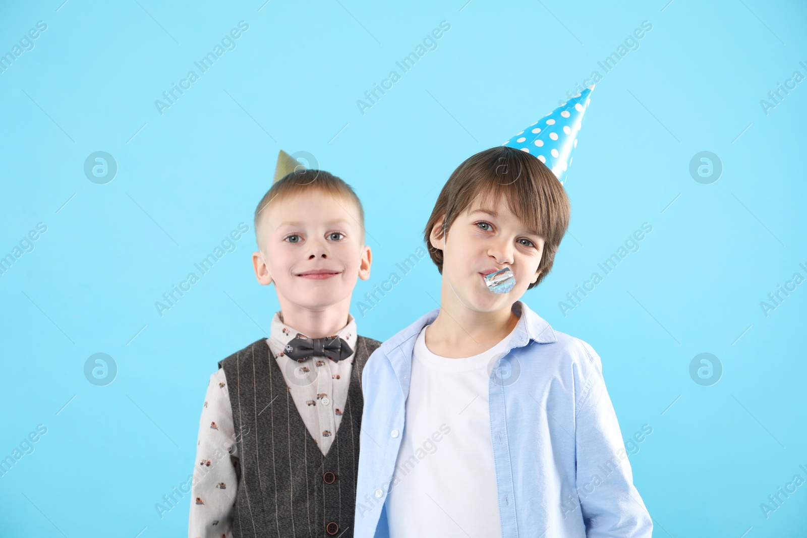 Photo of Children in conical paper hats with blower on light blue background. Birthday surprise party