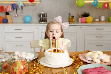 Photo of Cute little girl blowing out candles on birthday cake indoors. Surprise party