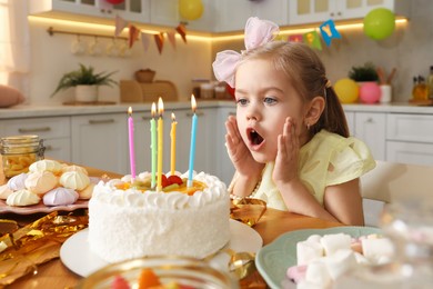 Photo of Cute little girl blowing out candles on birthday cake indoors. Surprise party