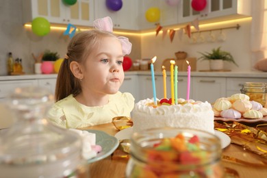 Photo of Cute little girl blowing out candles on birthday cake indoors. Surprise party