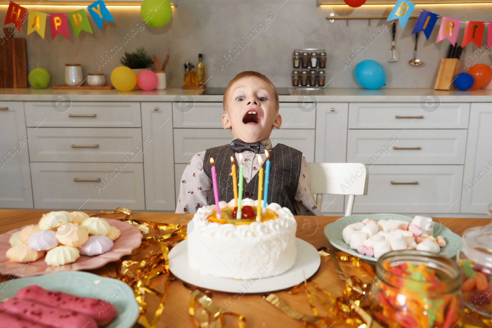 Photo of Cute little boy blowing out candles on birthday cake indoors. Surprise party