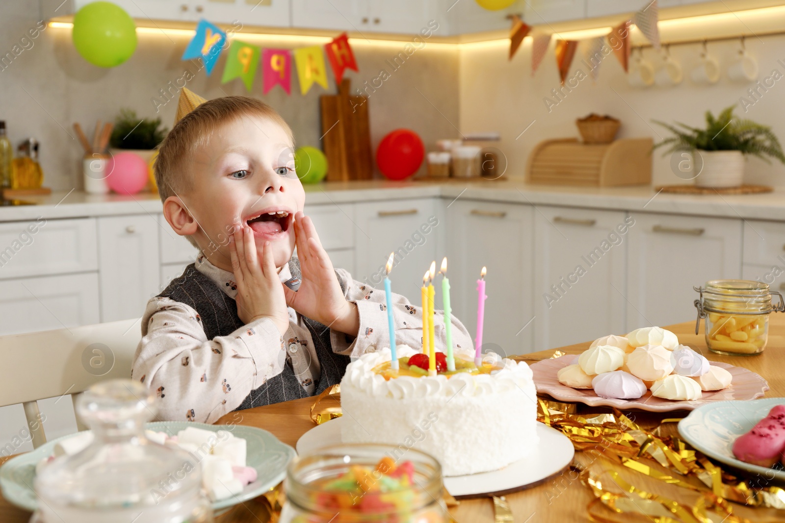 Photo of Cute little boy blowing out candles on birthday cake indoors. Surprise party