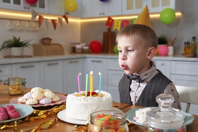 Photo of Cute little boy blowing out candles on birthday cake indoors. Surprise party