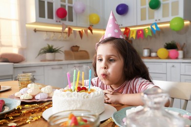 Photo of Cute little girl blowing out candles on birthday cake indoors. Surprise party