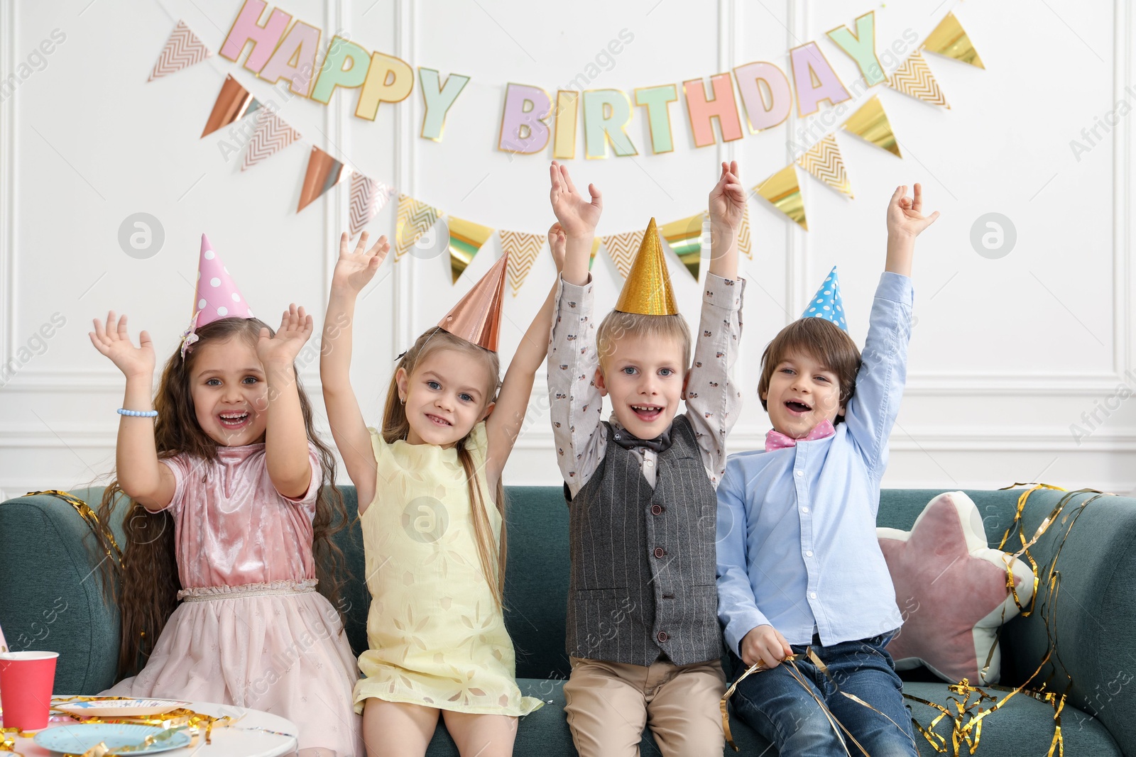 Photo of Children in conical paper hats celebrating birthday indoors. Surprise party