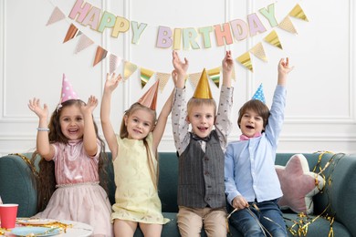 Photo of Children in conical paper hats celebrating birthday indoors. Surprise party