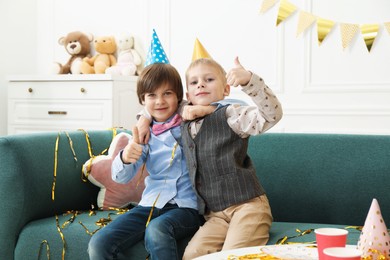 Photo of Children in conical paper hats showing thumbs up indoors. Surprise party