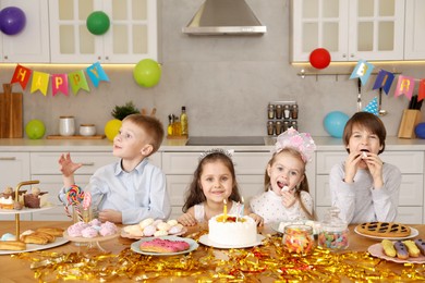 Photo of Children at table with tasty cake and different treats indoors. Surprise party