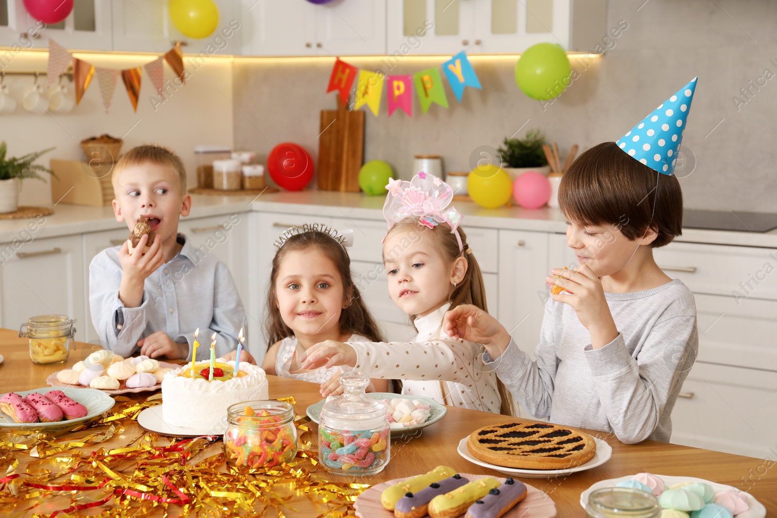 Photo of Children at table with tasty cake and different treats indoors. Surprise party