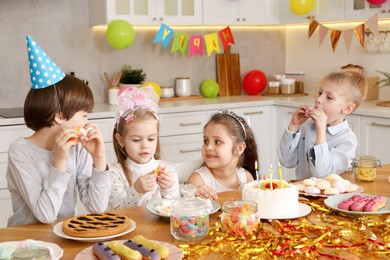 Photo of Children at table with tasty cake and different treats indoors. Surprise party