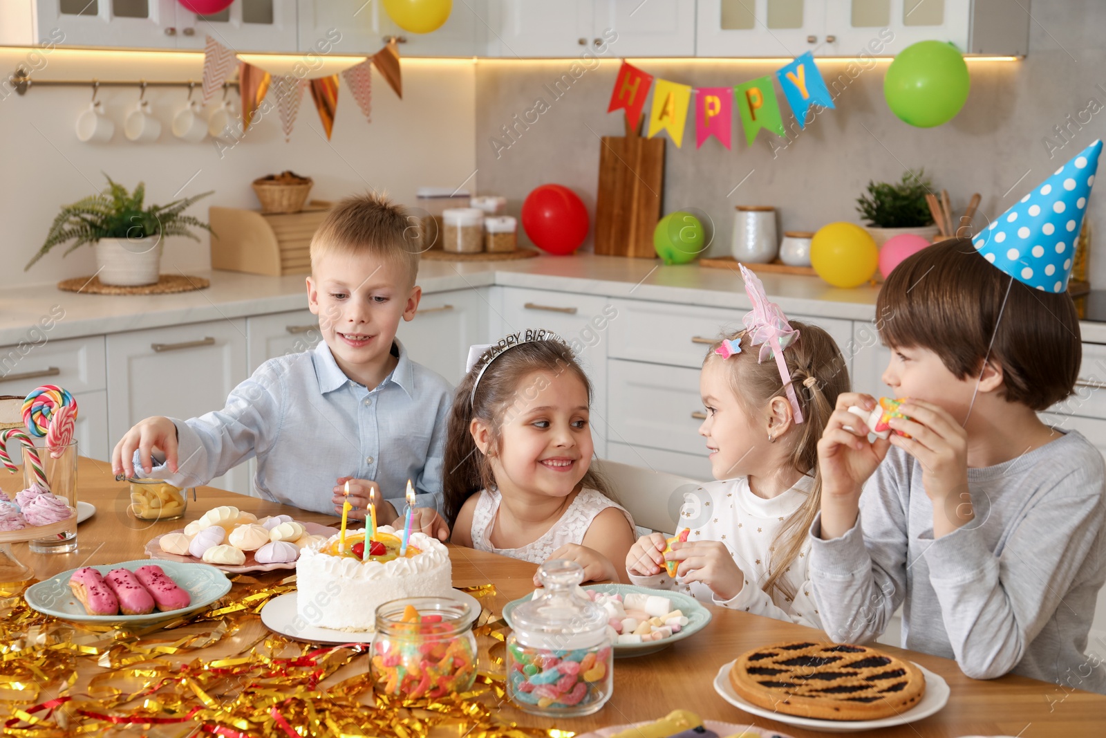 Photo of Children at table with tasty cake and different treats indoors. Surprise party