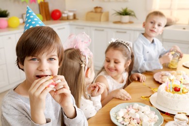 Photo of Children at table with tasty cake and different treats indoors, selective focus. Birthday surprise party