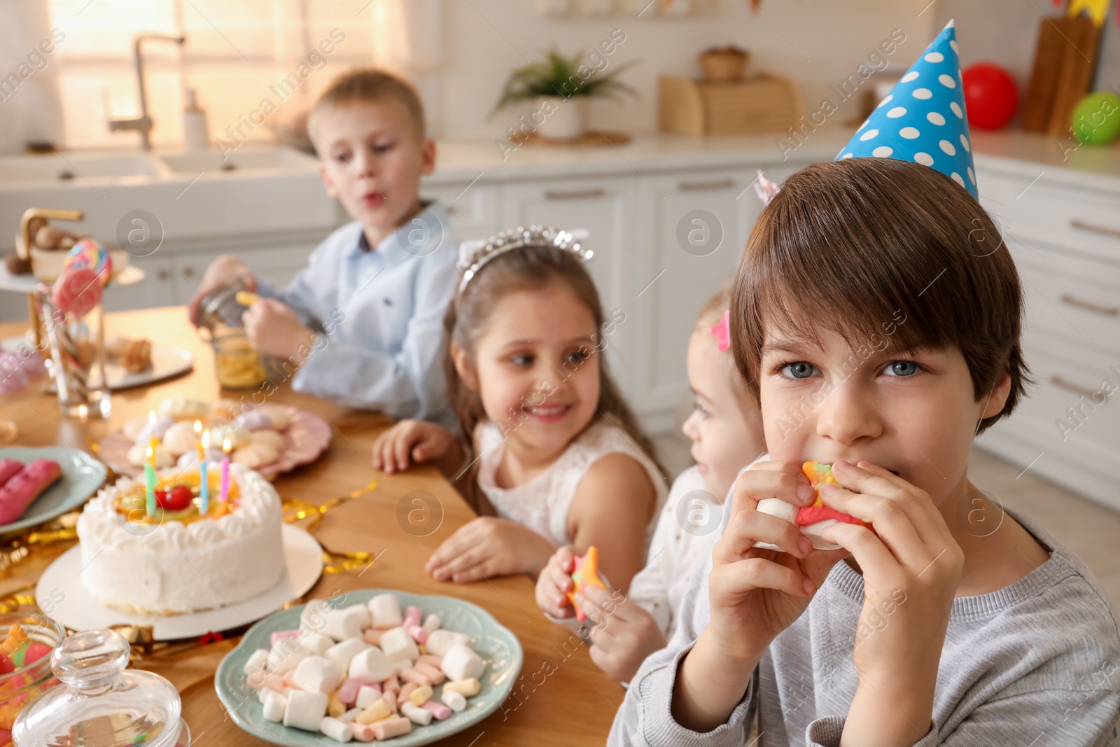 Photo of Children at table with tasty cake and different treats indoors, selective focus. Birthday surprise party