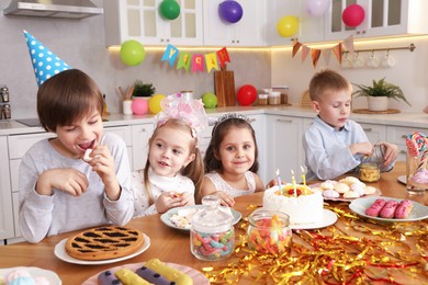 Photo of Children at table with tasty cake and different treats indoors. Surprise party