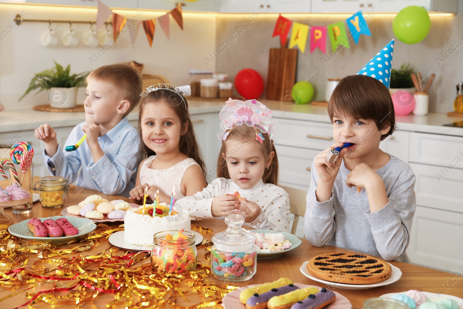 Photo of Children at table with tasty cake and different treats indoors. Surprise party