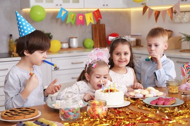 Photo of Children at table with tasty cake and different treats indoors. Surprise party