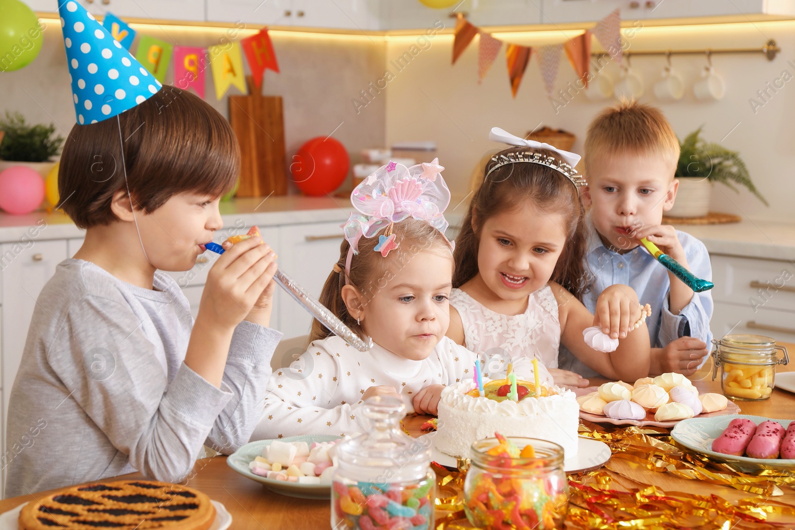 Photo of Children at table with tasty cake and different treats indoors. Surprise party