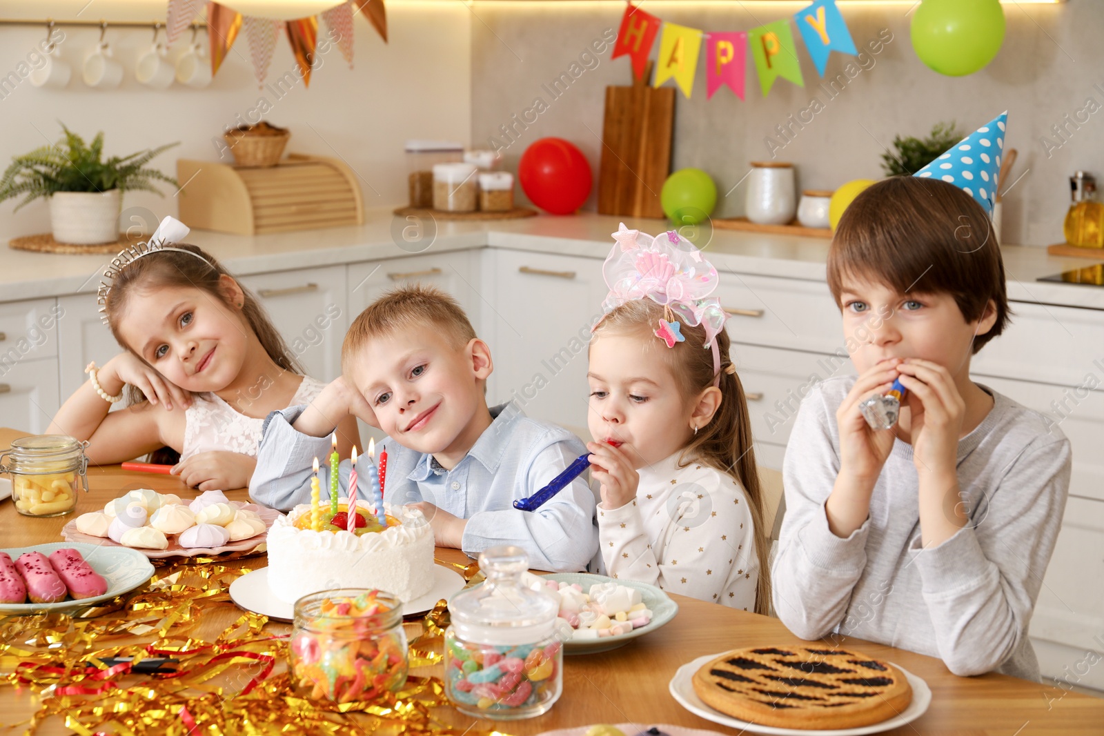 Photo of Children at table with tasty cake and different treats indoors. Surprise party