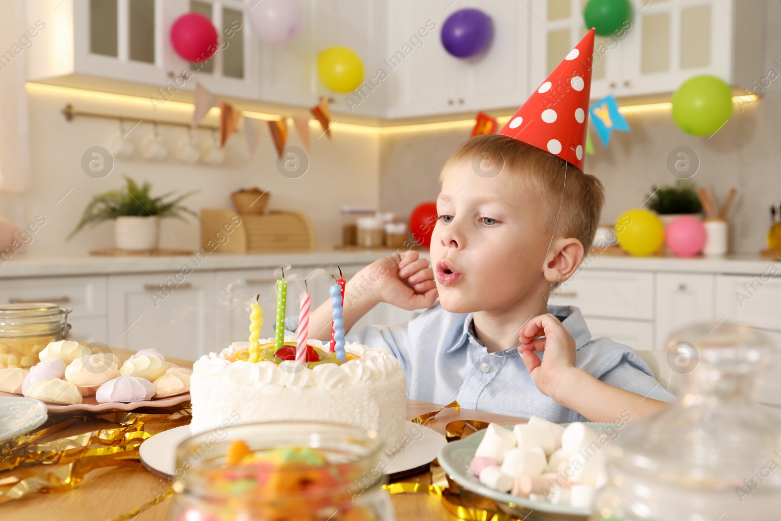 Photo of Cute little boy blowing out candles on birthday cake indoors. Surprise party