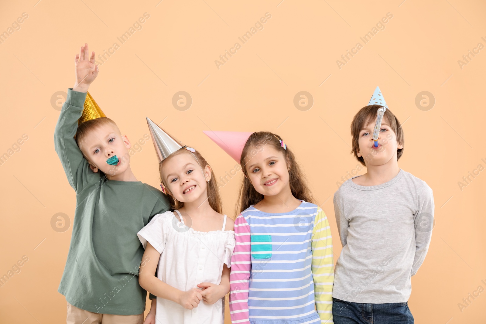 Photo of Children in conical paper hats with blowers on beige background. Birthday surprise party