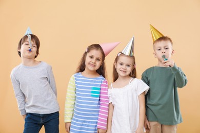 Photo of Children in conical paper hats with blowers on beige background. Birthday surprise party