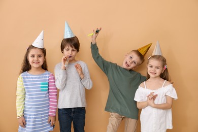 Photo of Children in conical paper hats with blowers on beige background. Birthday surprise party