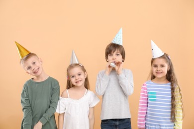 Photo of Children in conical paper hats with blowers on beige background. Birthday surprise party