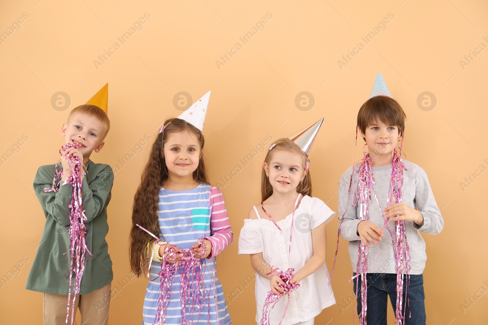 Photo of Children in conical paper hats with streamers on beige background. Birthday surprise party