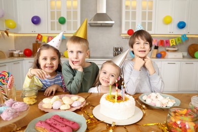 Photo of Children at table with tasty cake and different treats indoors. Birthday surprise party