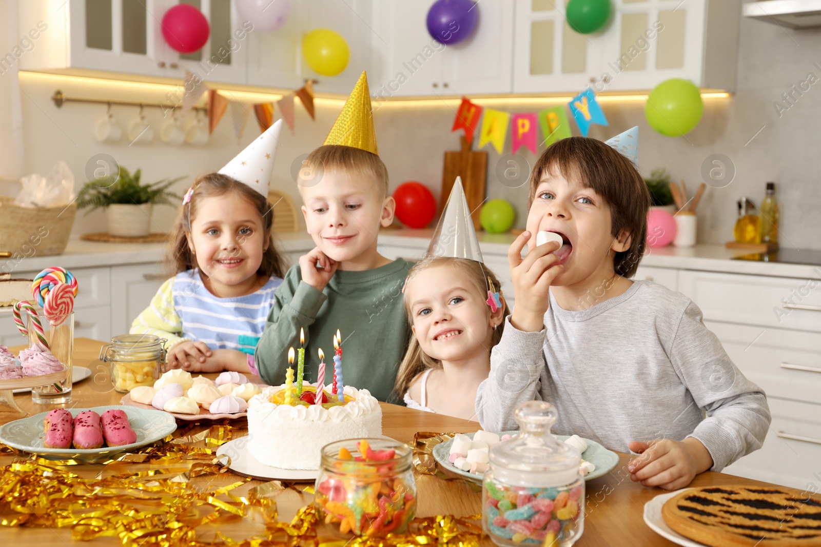 Photo of Children at table with tasty cake and different treats indoors. Birthday surprise party