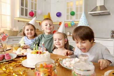 Photo of Children at table with tasty cake and different treats indoors. Birthday surprise party