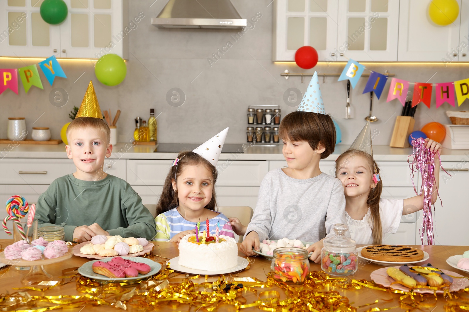 Photo of Children at table with tasty cake and different treats indoors. Birthday surprise party