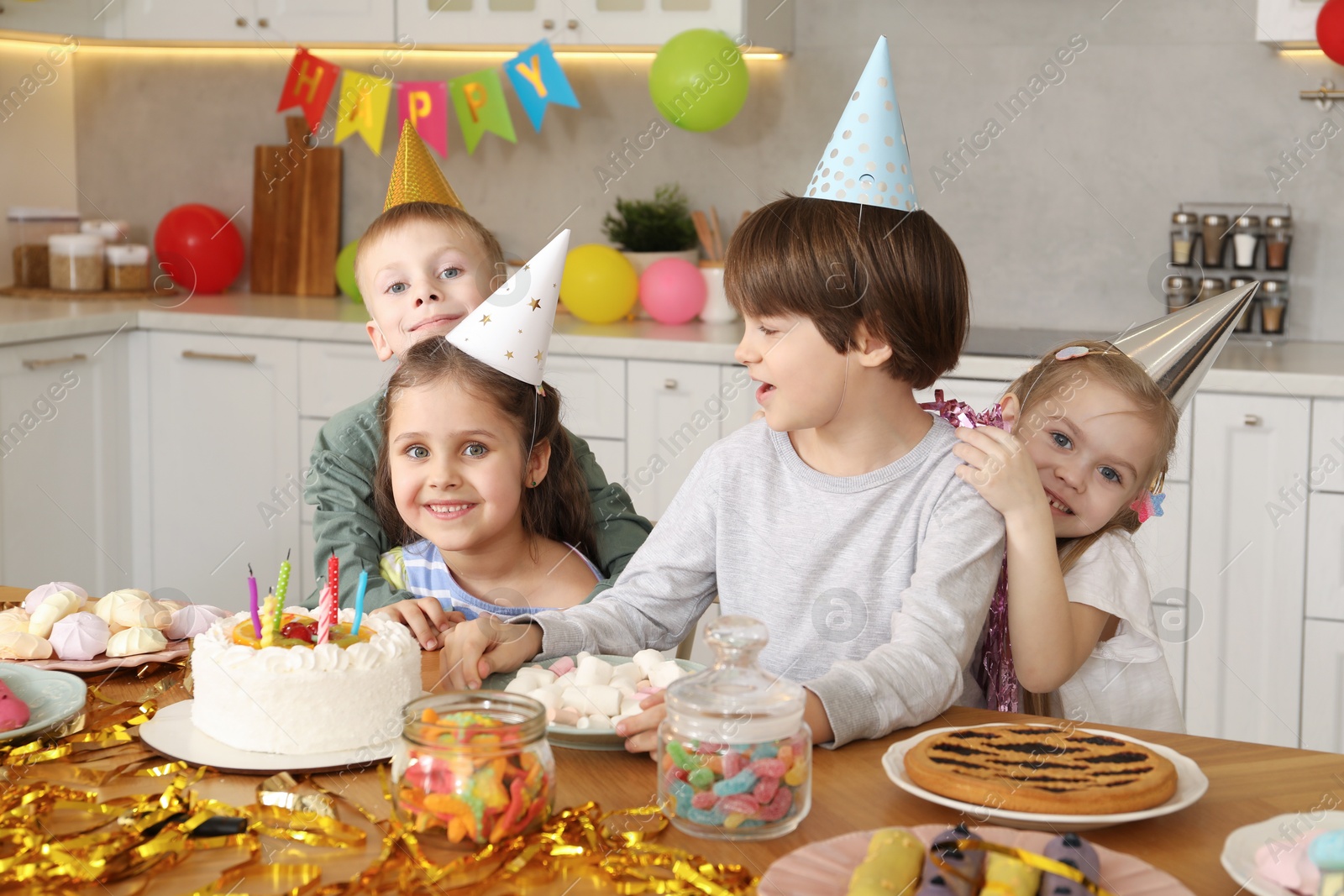 Photo of Children at table with tasty cake and different treats indoors. Birthday surprise party