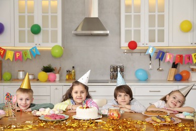 Photo of Children at table with tasty cake and different treats indoors. Birthday surprise party