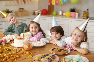 Photo of Children at table with tasty cake and different treats indoors, selective focus. Birthday surprise party