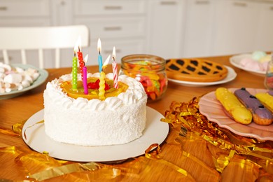 Photo of Tasty cake with burning candles and different treats on table indoors. Birthday surprise party