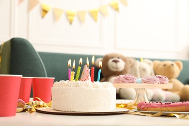 Photo of Tasty cake with burning candles and different treats on table indoors. Birthday surprise party