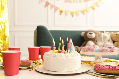 Photo of Tasty cake with burning candles and different treats on table indoors. Birthday surprise party