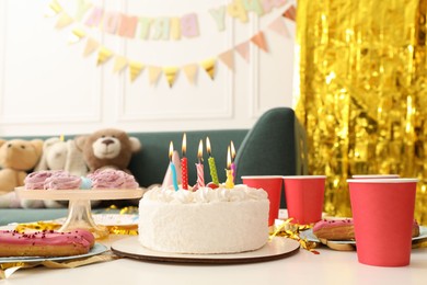 Photo of Tasty cake with burning candles and different treats on table indoors. Birthday surprise party