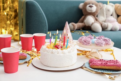 Photo of Tasty cake with burning candles and different treats on table indoors. Birthday surprise party