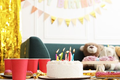 Photo of Tasty cake with burning candles and different treats on table indoors. Birthday surprise party